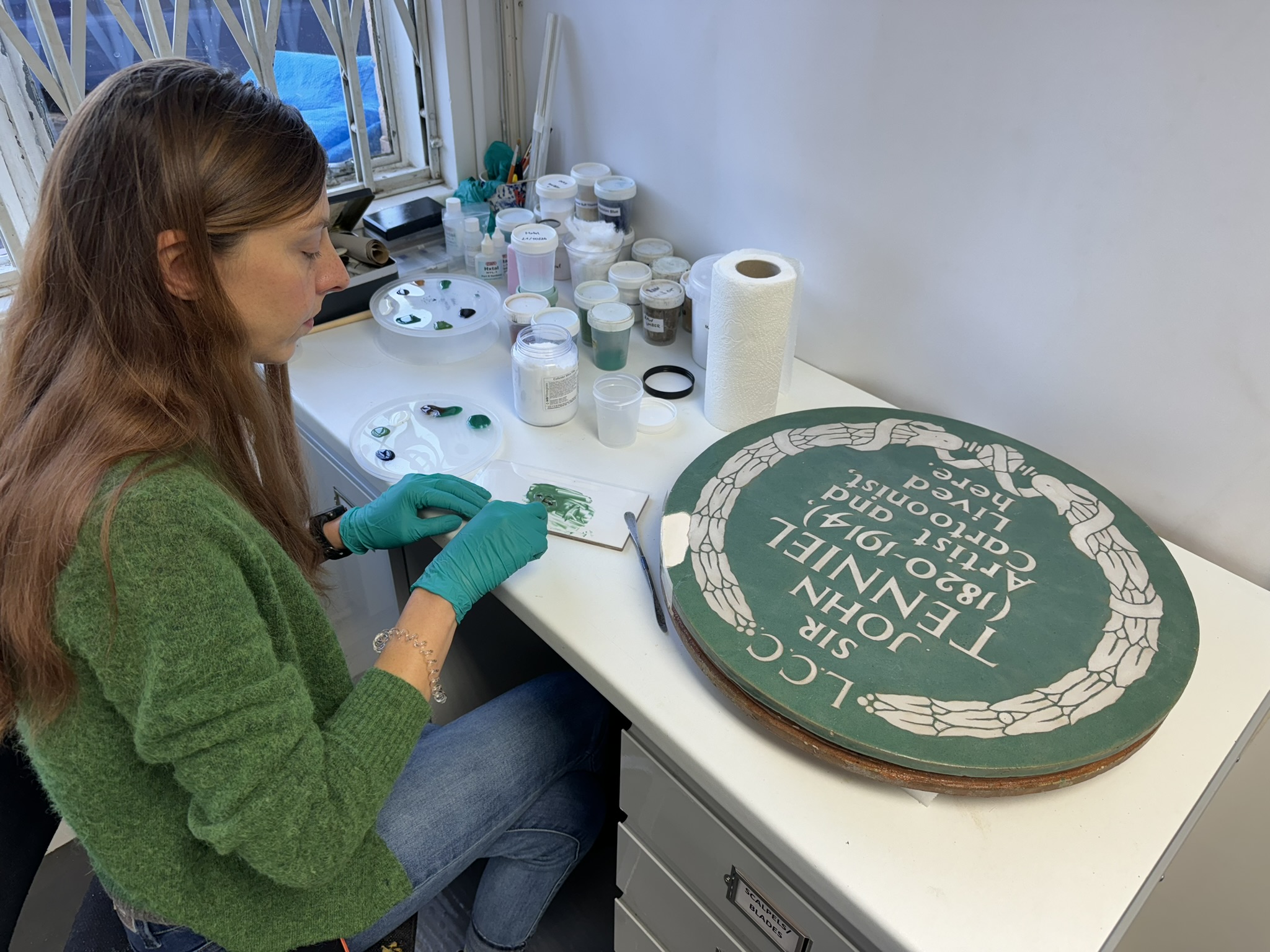 Image: a conservator works on the historic plaque to Sir John Tenniel