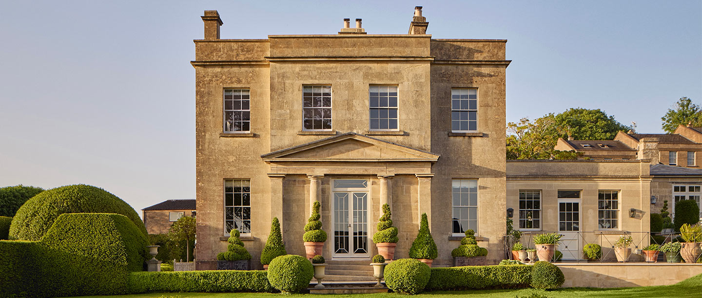 A large manor house built from sandy coloured Bath stone behind a lush green lawn