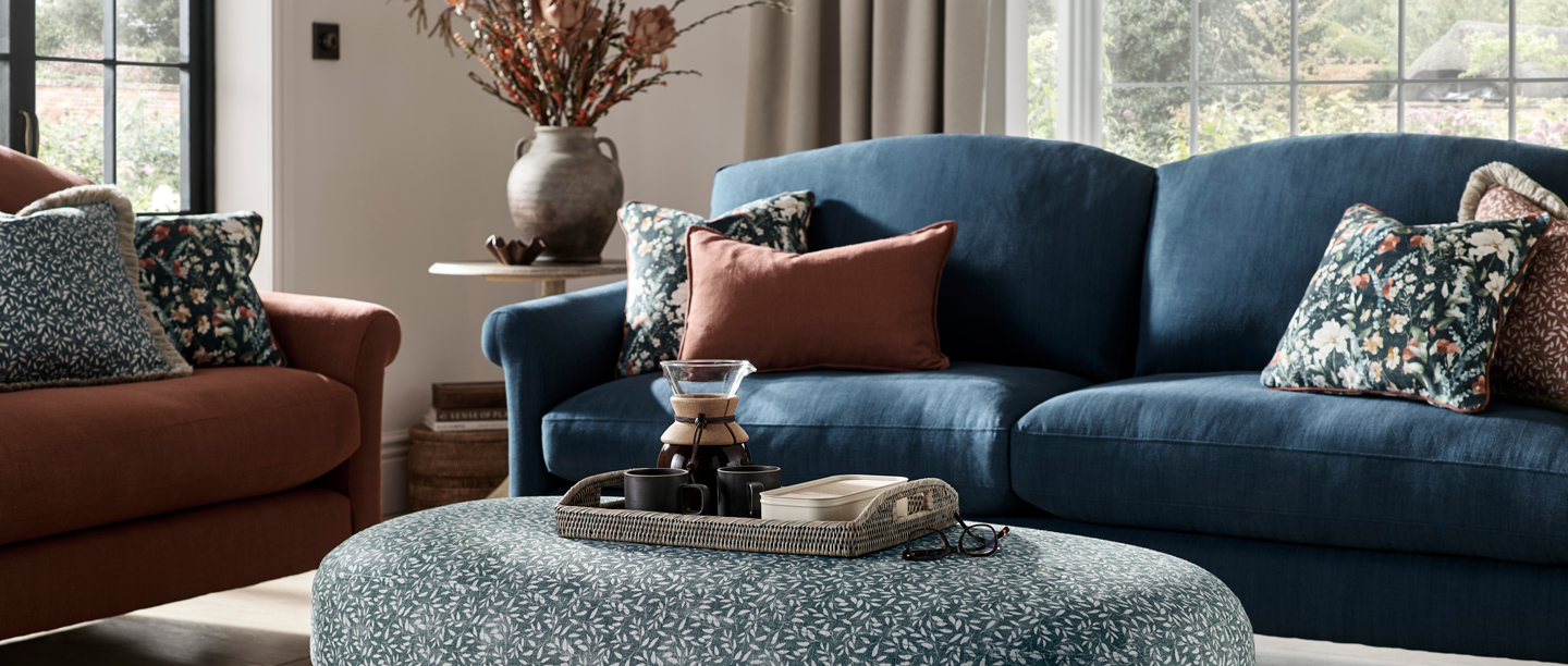 A photo of the Branded Furniture Company patterned sofas and blue footstall with a vase of flowers in the background.