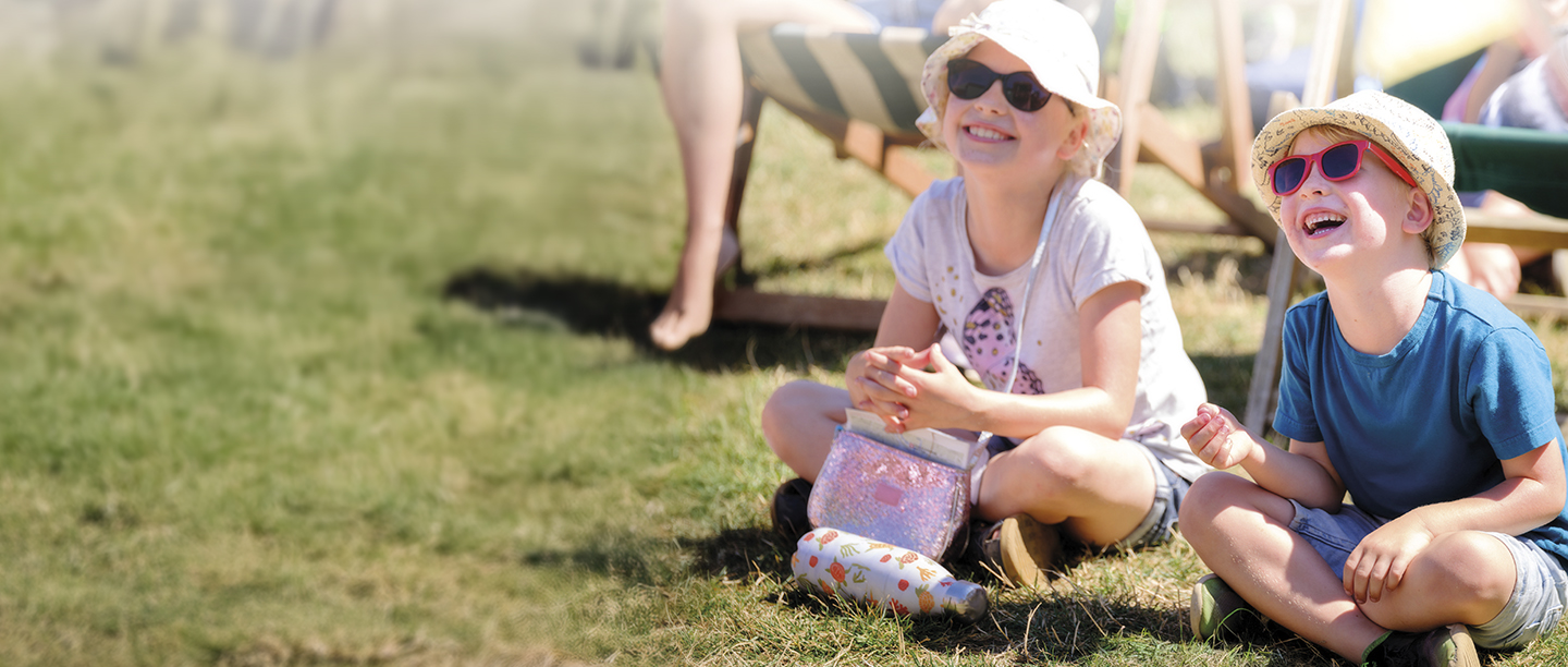 Two children sit laughing in sunglasses and sunhats