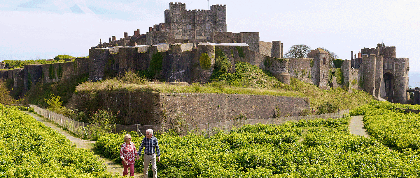 Photo of two people walking beyond the spur in front of Dover Castle in the summer