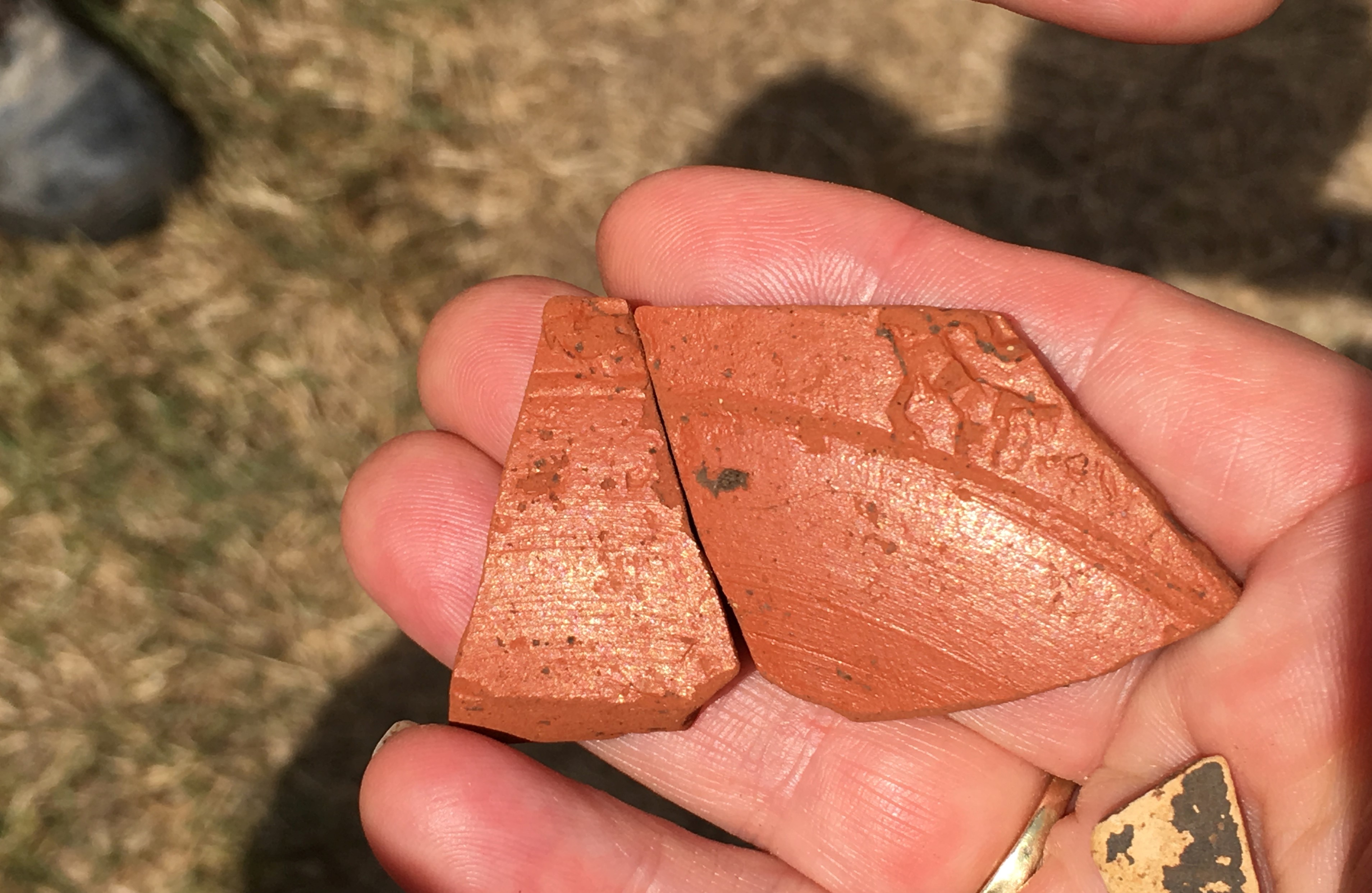 Two pieces of broken burnt orange-coloured pottery with some decoration carved into them.