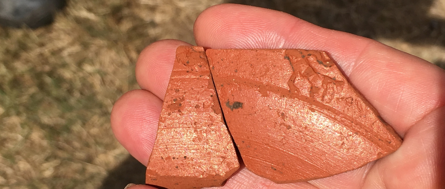 Two pieces of broken burnt orange-coloured pottery with some decoration carved into them.