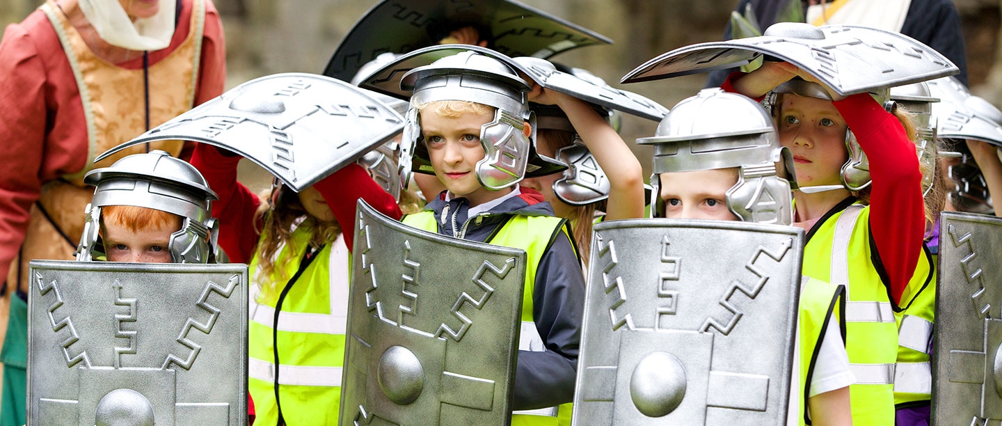 Students dressed in Roman helmets and holding Roman shields in a protective shell formation