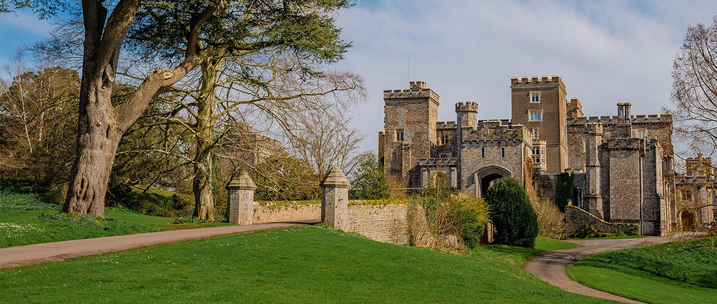 A grand looking castle with square turrets seen across a lawn