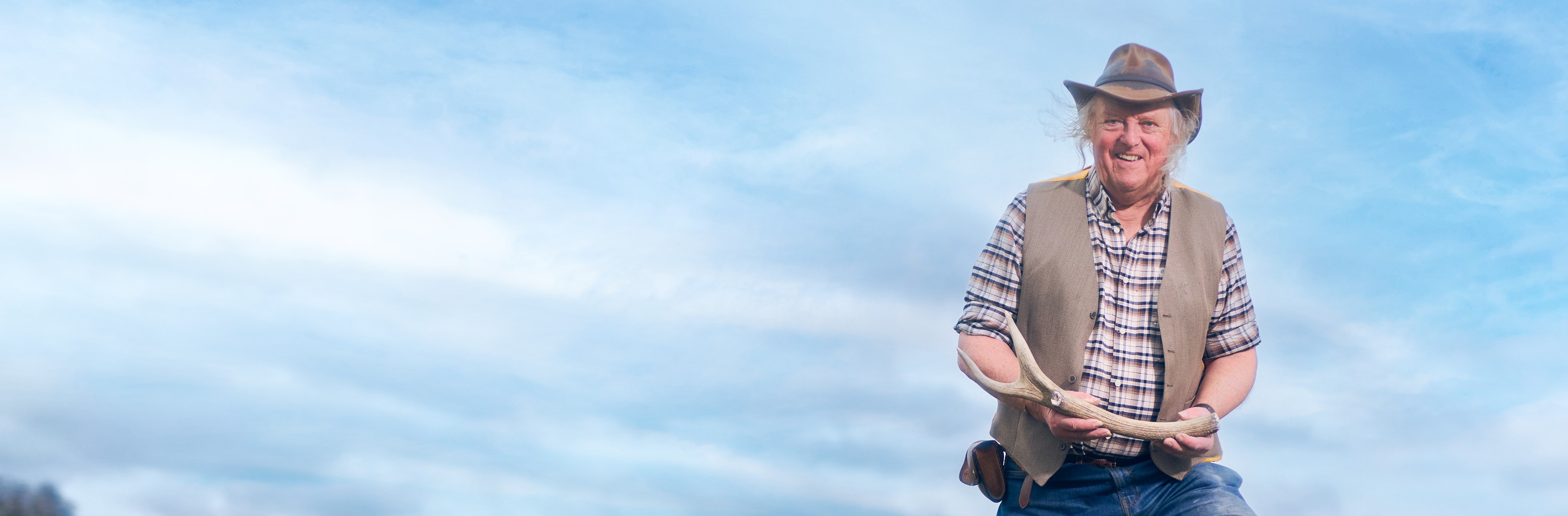 Photo of a man wearing a hat, waistcoat and checked shirt and holding an antler