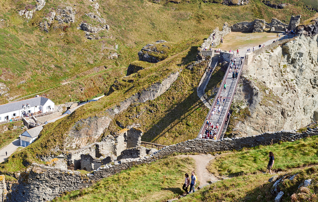 A view of Tintagel Castle showing the stone ruins, new bridge connecting the island to the mainland and steps up to the ruins A view of Tintagel Castle showing the stone ruins, new bridge connecting the island to the mainland and steps up to the ruins