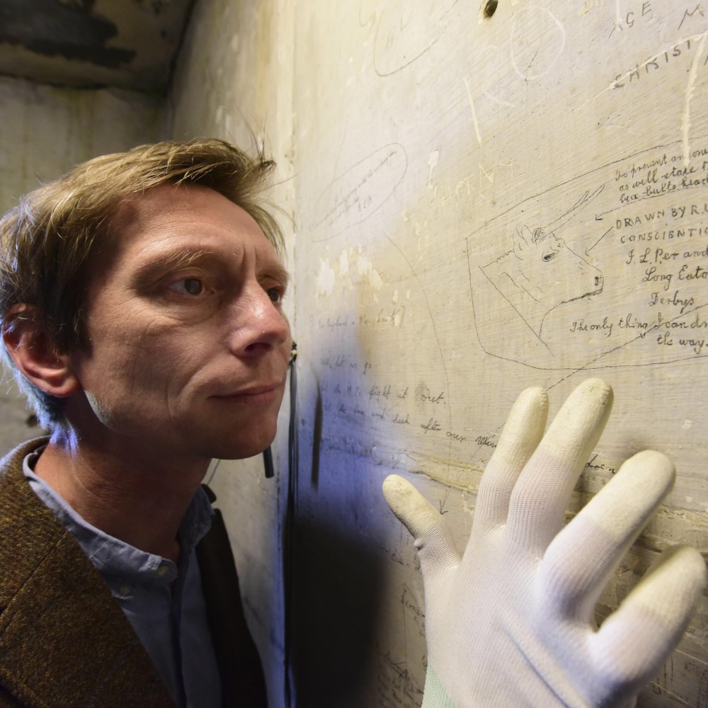 Photo of someone examining First World War graffiti on the wall of a cell block at Richmond Castle