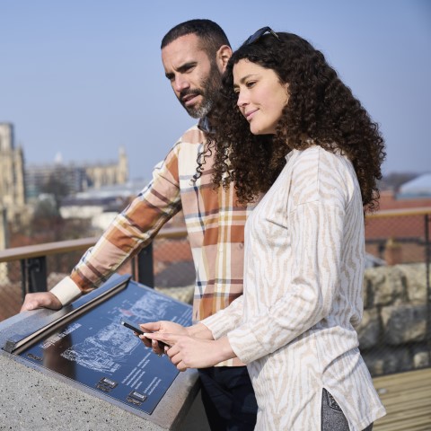 Photo of two people reading an interpretation panel and looking out across York on the roof of Clifford's Tower