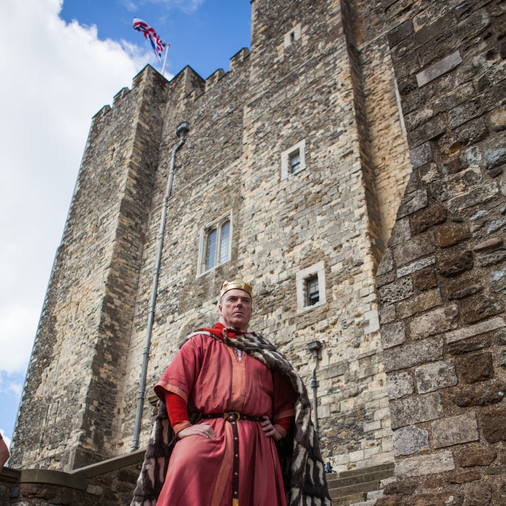 Photo of a historical interpreter dressed as a king standing in front of the Great Tower at Dover Castle