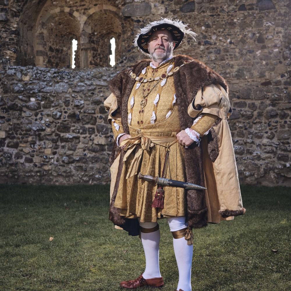 Photo of a historical interpreter dressed as Henry VIII standing in front of a castle wall