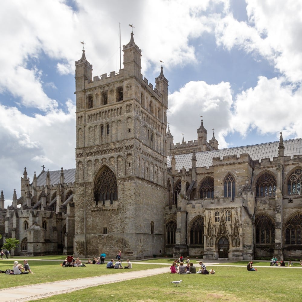 Photo of Exeter Cathedral on a sunny day with people sat on the grass outside