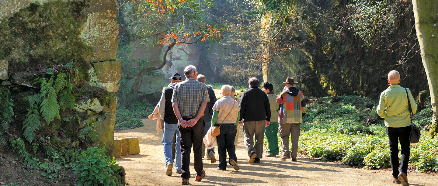 A group of people on a guided tour in Belsay Hall's Gardens in the sunshine.