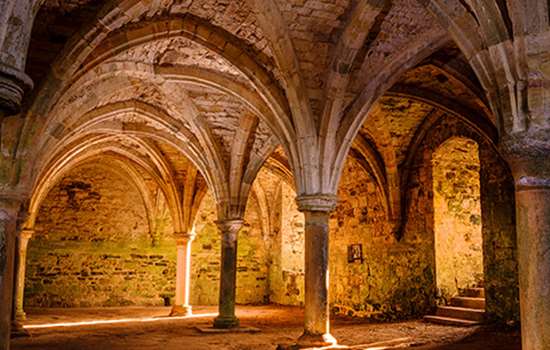A room with lots of stone arches and a vaulted ceiling with a warm orange glow as sunlight creeps in a window A room with lots of stone arches and a vaulted ceiling with a warm orange glow as sunlight creeps in a window