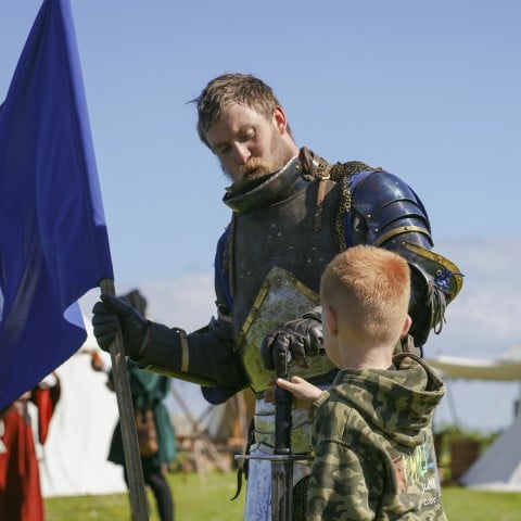 Photo of a person dressed as a knight showing a child their sword