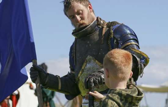 Photo of a person dressed as a knight showing a child their sword