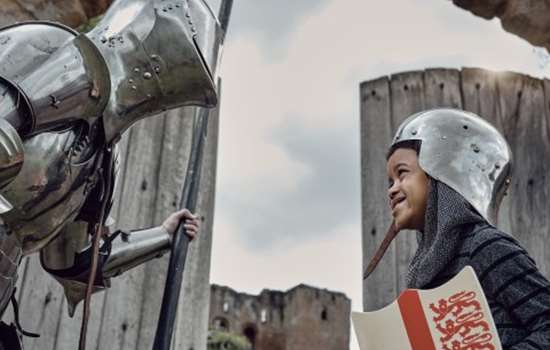 Photo of a child dressed as a knight looking at an adult in a suit or armour with Kenilworth Castle in the background