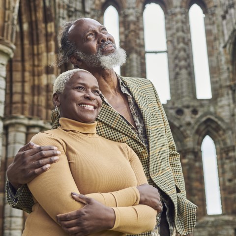 Photo of two people smiling as they look at the ruins of Whitby Abbey