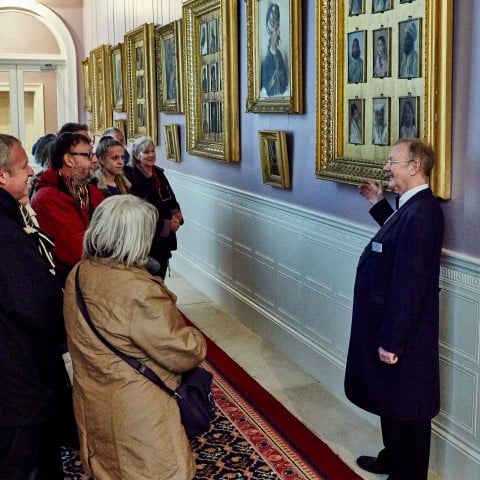 Photo of an English Heritage tour guide speaking to a group of people in a room of paintings in Osborne House on the Isle of Wight