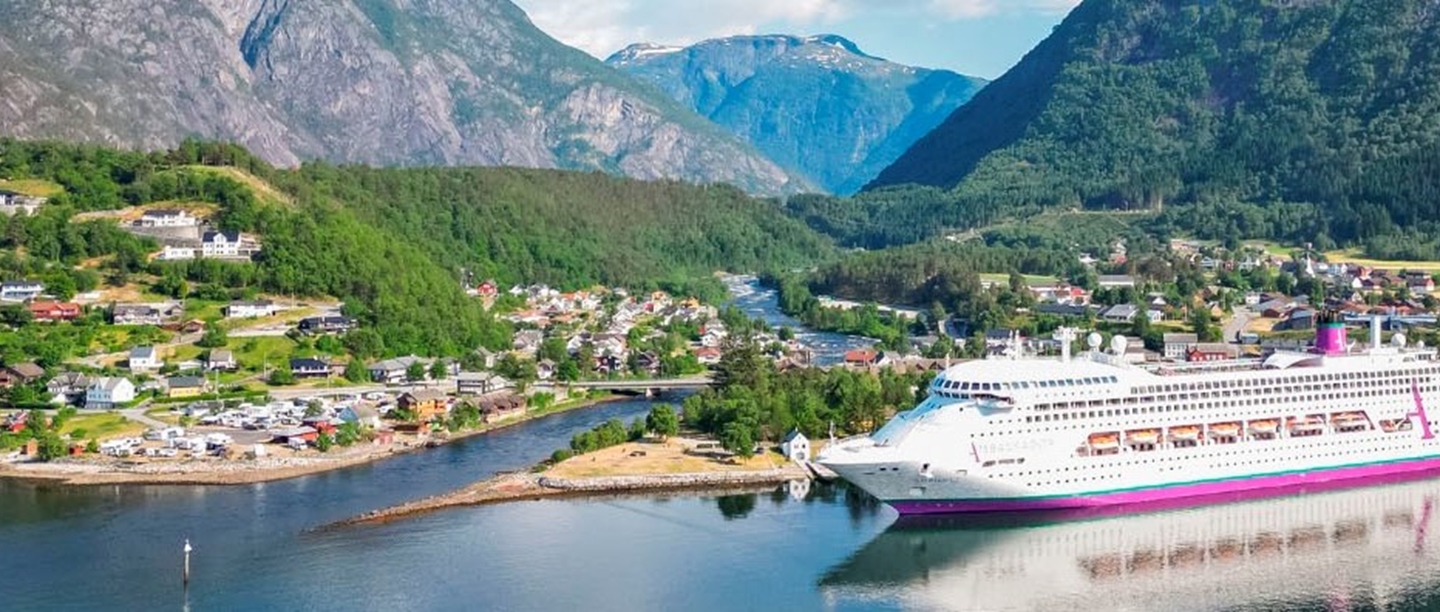 Photo of an Ambassador cruise ship next to a coastal town with mountains in the background