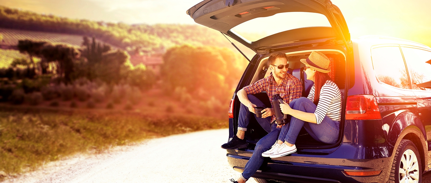 Photo of two people sat in the boot of a car on a sunny day