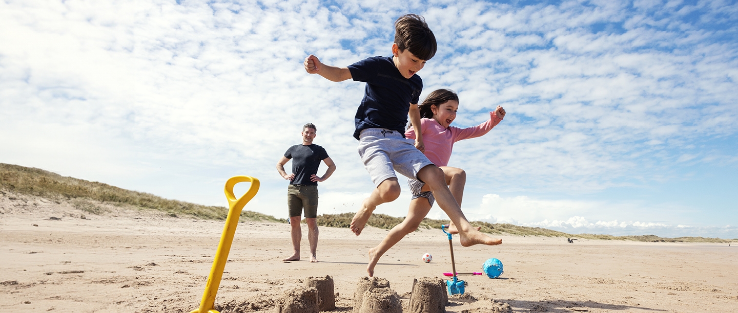 Photo of two young children jumping over sandcastles on a beach