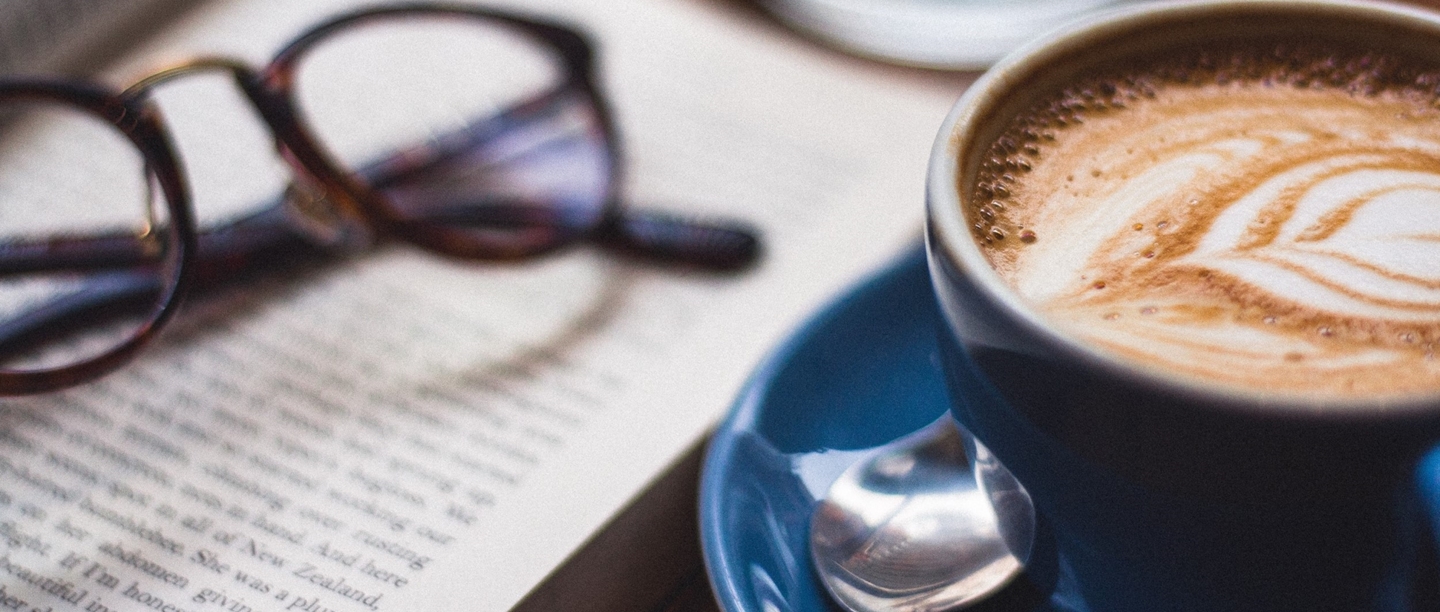 Photo of a cup of coffee next to a book and a pair of glasses