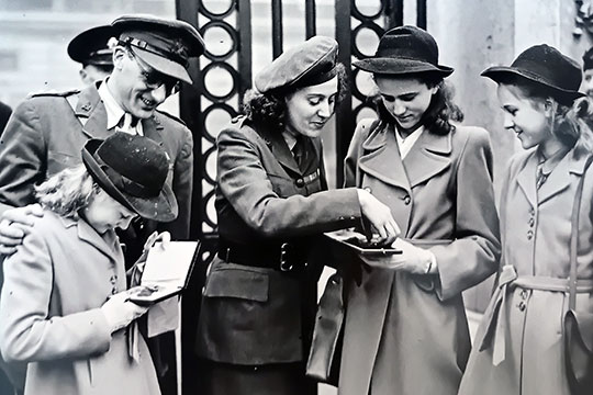 Black and white photograph of Sansom with her children, looking at her medals outside the gates of Buckingham Palace Black and white photograph of Sansom with her children, looking at her medals outside the gates of Buckingham Palace