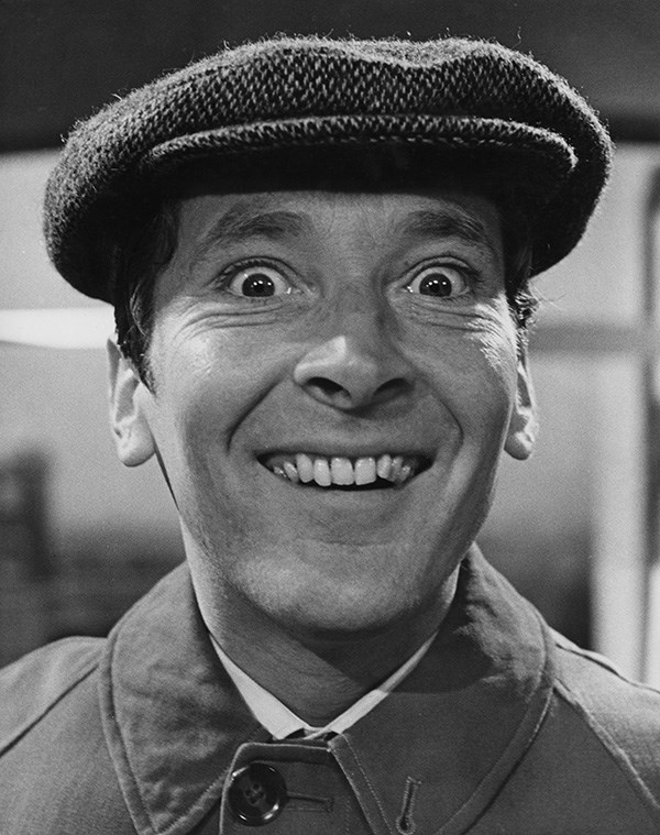 Black and white photograph of Kenneth Williams grinning broadly at camera