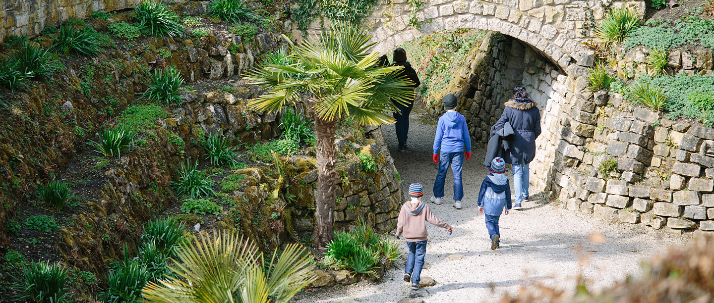 A group of adults with young children walk in the gardens at Brodsworth Hall dressed in winter coats and hats.