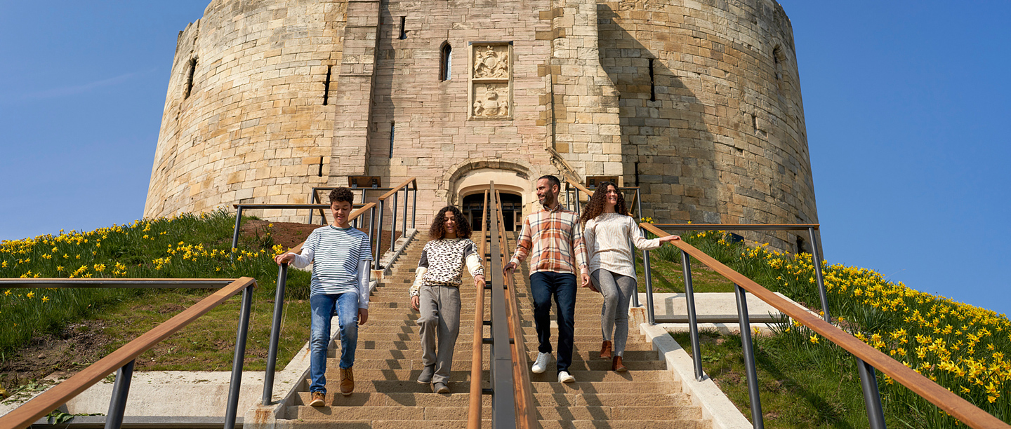 Two adults and two children walk down the steps at Clifford's Tower in York. There are daffodils growing on the mound.