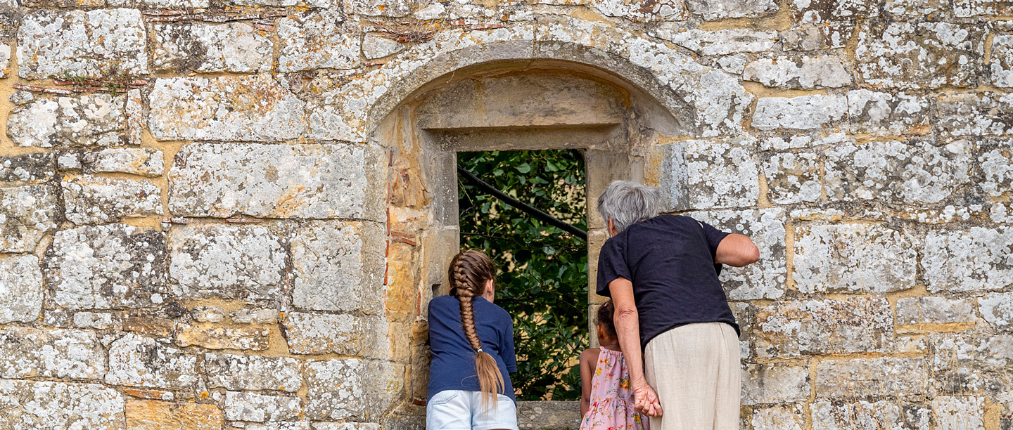 An adult and two children look through a stone arch window at Bayham Old Abbey. 