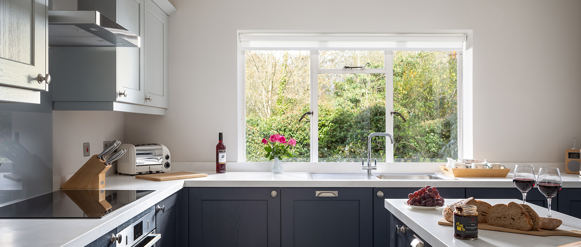 A modern holiday cottage kitchen with two glasses of red wine and a loaf of cut bread on the counter. 