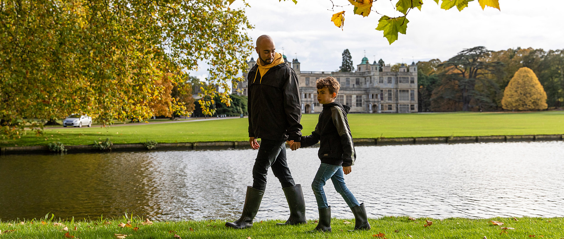 A man and a child walk and hold hands in gardens of Audley End in the autumn.