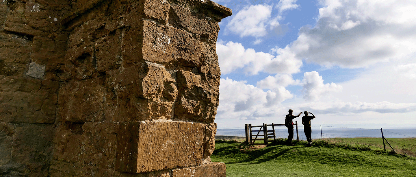 Photo of two people in winter clothing looking out to sea next to St Catherine's Chapel in Abbotsbury on a sunny day