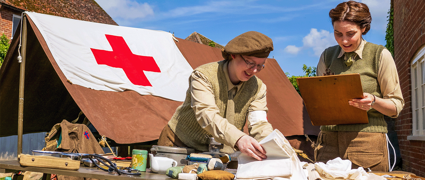 Photo of two people dressed in Second World War clothing arranging medical items from the period on a table