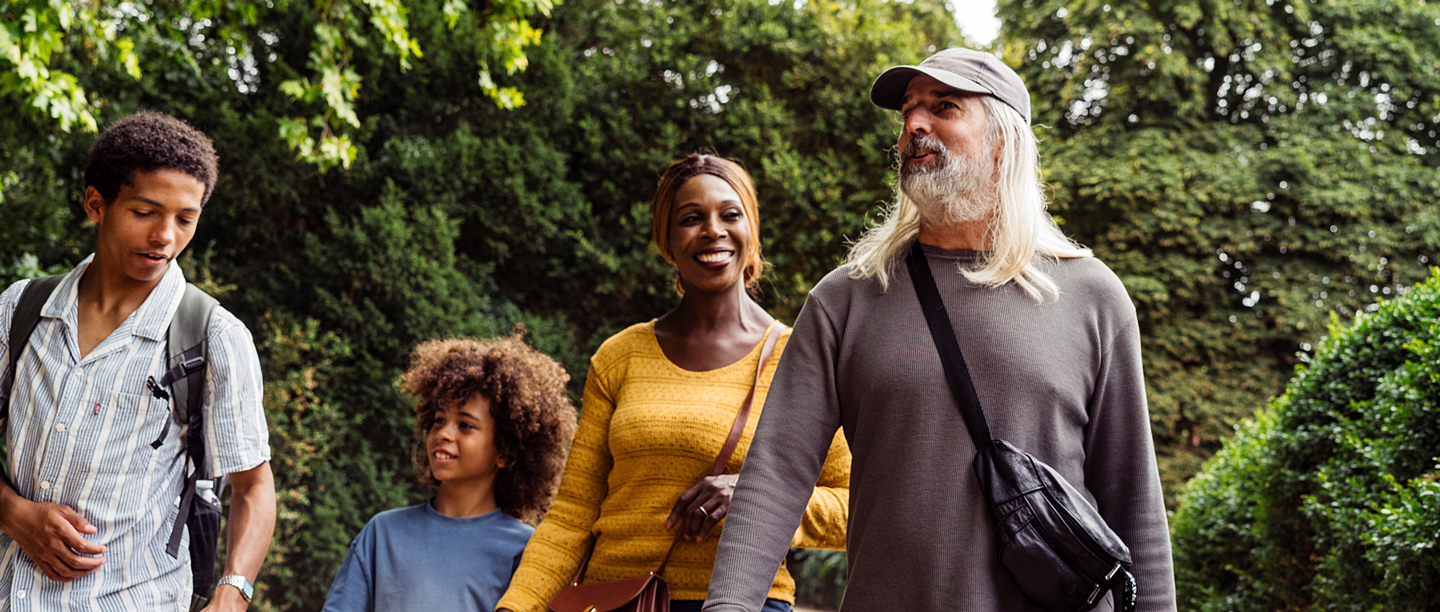 Two adults, one teenager and a younger child walk through a wooded area smiling.
