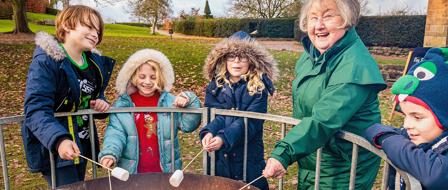 Photo of an adult and four children toasting marshmallows around a fire pit at Kenilworth Castle and Elizabethan Garden