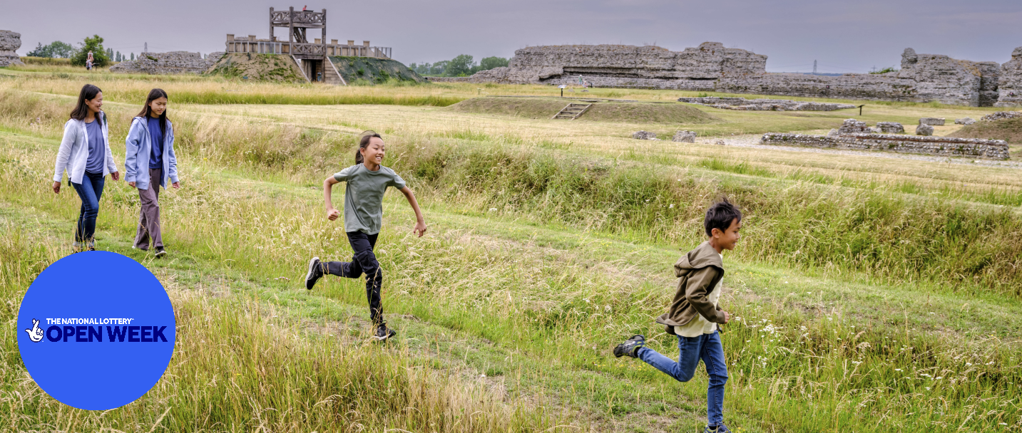 Photo of an adult and three children walking and running through a field at Richborough Roman Fort