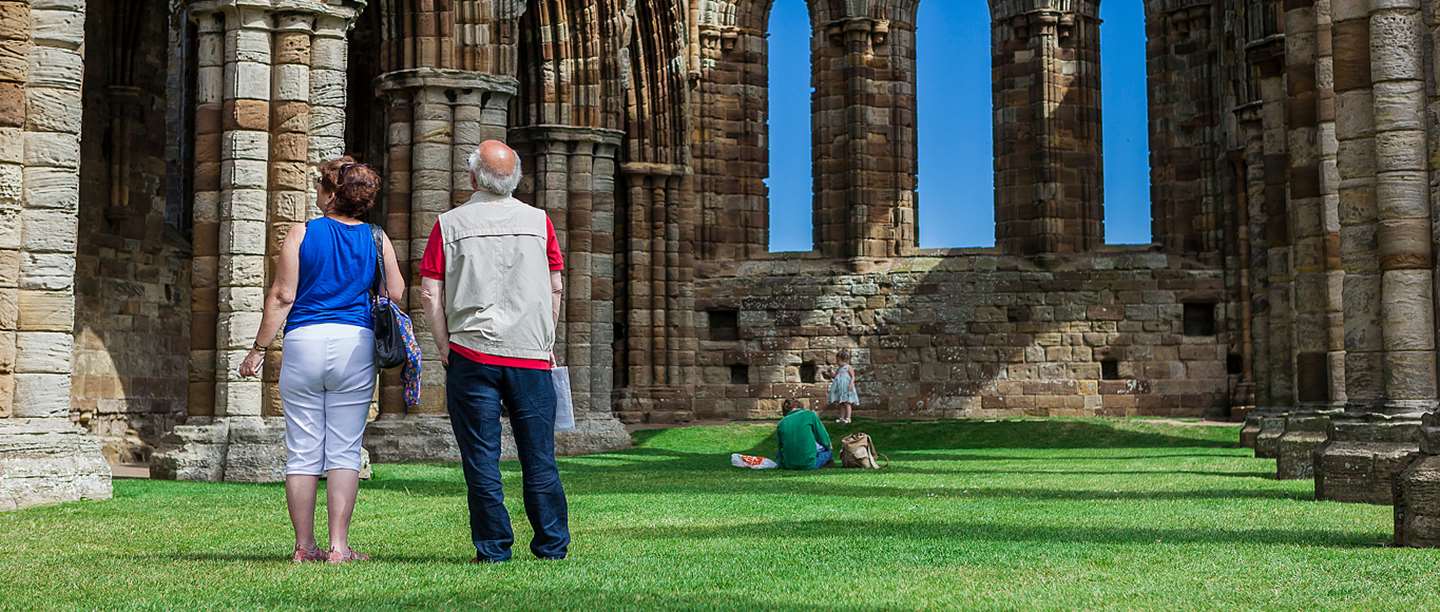 Photo of two people standing and looking up at the remains of an abbey