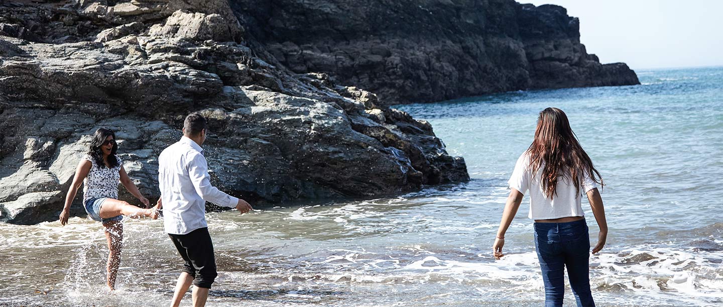 Three people splash in the shallows on a beach by a rocky headland