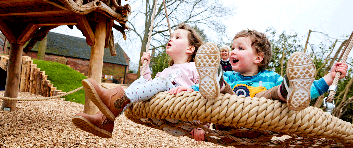Image: children are playing on a large round swing in the play area