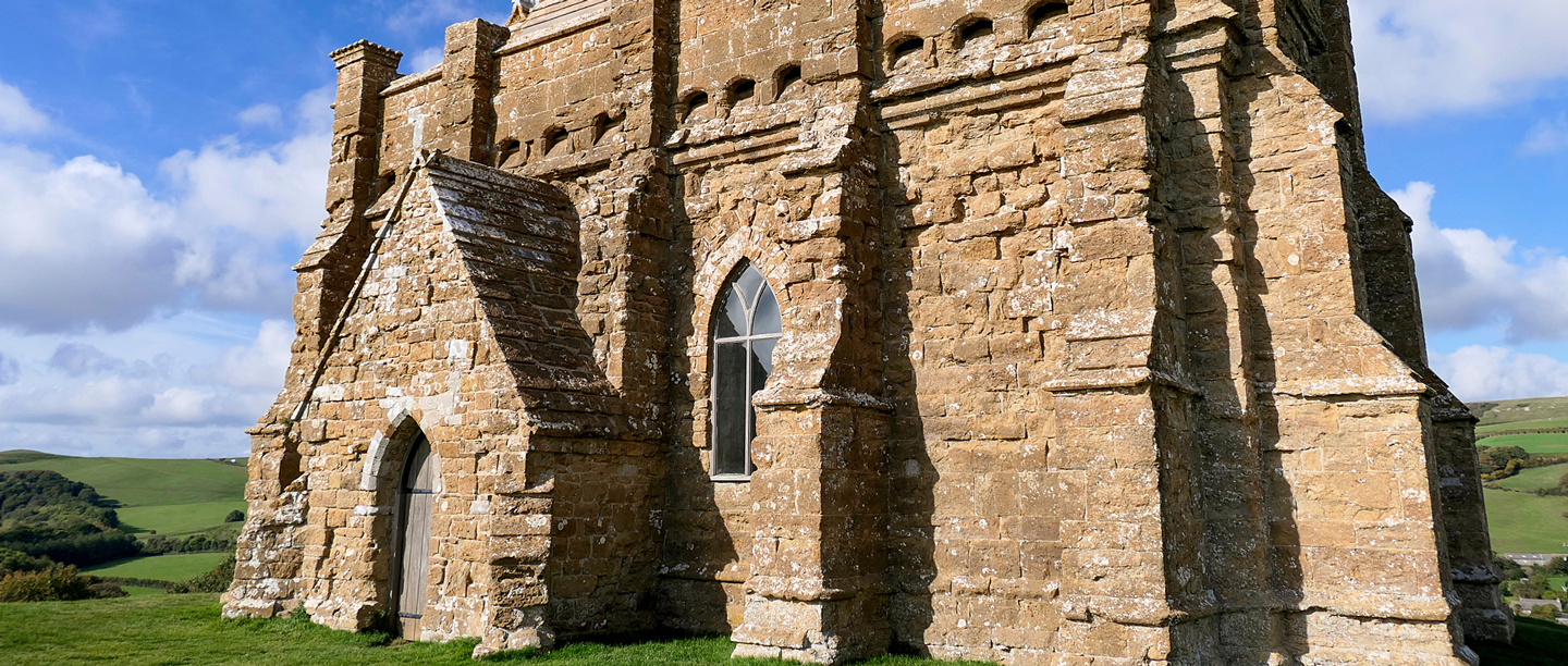A close-up view of the stone St Catherine's Chapel with an arched wooden door and window. 