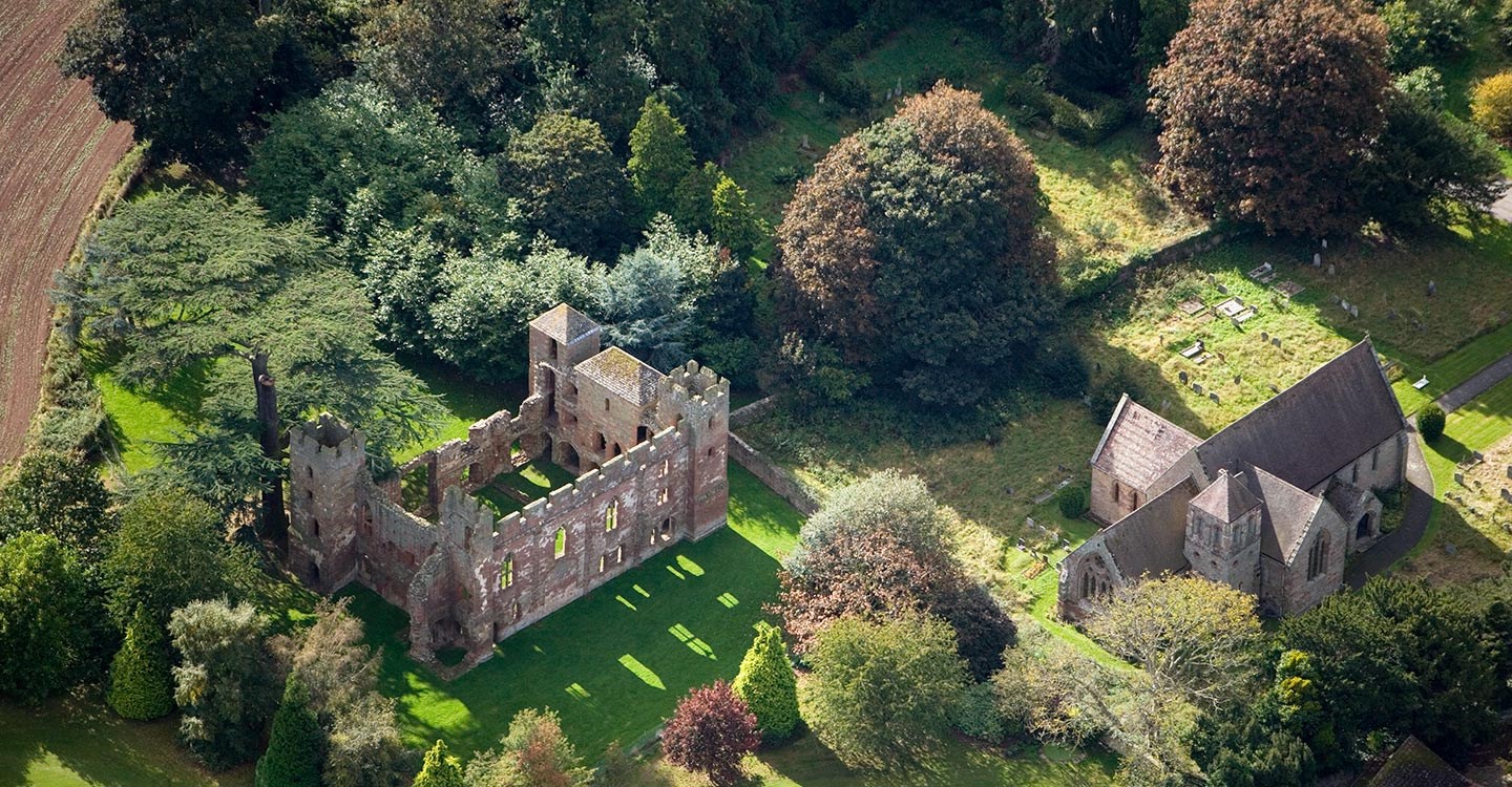 Aerial view of Acton Burnell Castle ruins alongside 13th century medieval St Mary's Church set amongst a rich planting of trees