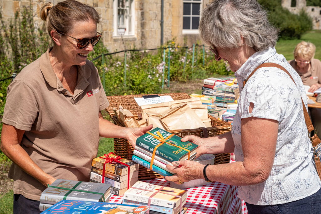 A volunteer helps a visitor browse second hands books outside in the sunshine at Bayham Old Abbey.