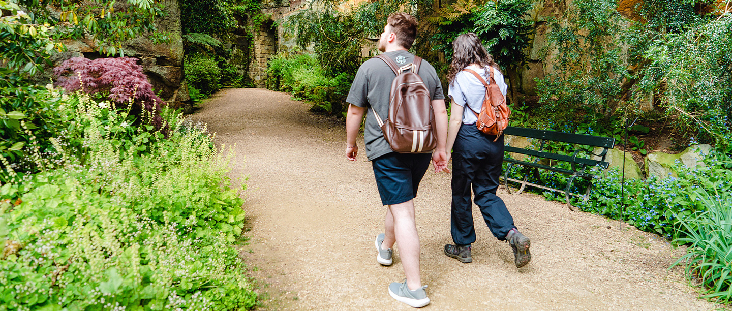 A man and a woman walk through the Quarry Gardens at Belsay Hall which are surrounded by plants and greenery.