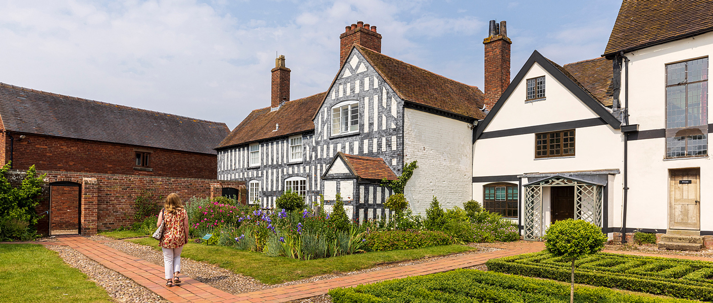 A woman stands looking at the exterior of Boscobel House on a sunny day.