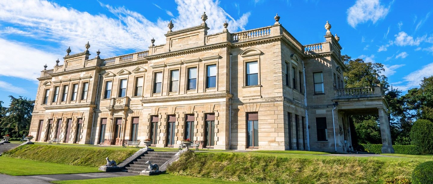 The exterior of Brosdworth Hall in the sunshine, underneath a blue sky.