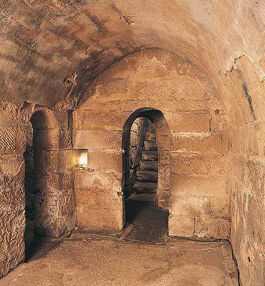 Interior of Hexham crypt with view through narrow arched doorway to steps leading up