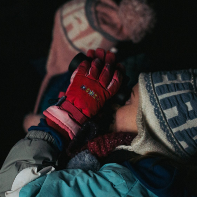 Two young people in winter clothing looking through binoculars at the night sky.